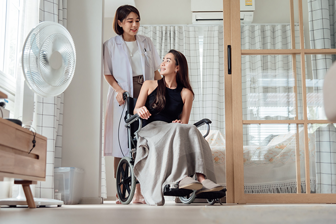 A female doctor or nurse is looking after a patient in a wheelchair.